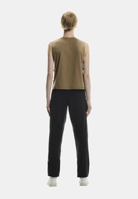 Hnedý top bez rukávov s rovnýcm strihom, skombinovaný s čiernymi, úzkymi nohavicami s hladkou textúrou a bielymi teniskami.