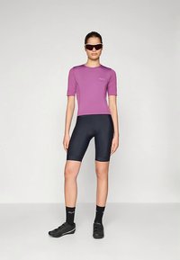 Violettes kurzärmliges Radtrikot mit Logo, kombiniert mit marineblauen Radhosen und schwarzen Schuhen. Sonnenbrille komplettiert den sportlichen Look.