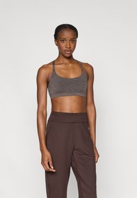 Γκρι αθλητικό σουτιέν με λαιμόκοψη scoop και λεπτές τιράντες, συνδυασμένο με παντελόνια ψηλόμεσα σε σκουρό καφέ χρώμα, που αναδεικνύουν μια λεία, εφαρμοστή υφή.