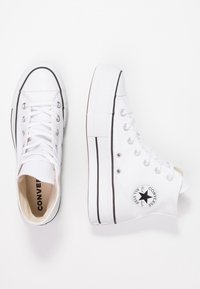 White high-top Converse sneakers with black trim, metal eyelets, and the classic star logo visible on the inner side of the right shoe.
