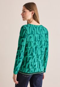Grönmönstrad långärmad topp med abstrakta former, slät textur, rundad halsringning och lätt elastik i nederkanten.