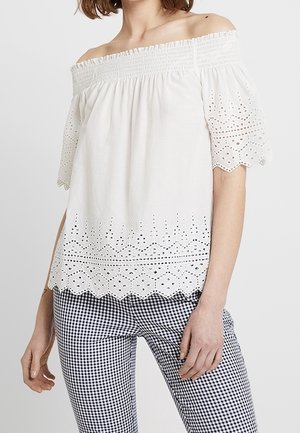 Top bianco scollato con maniche a sbuffo corte, con dettagli in pizzo occhiellato e orlo scallopato. Abbinato a pantaloni a motivo vichy.