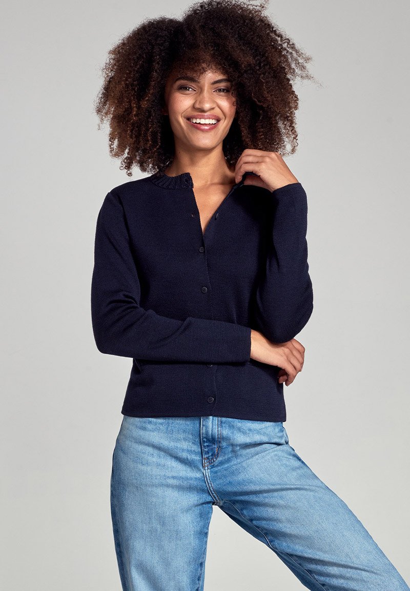 Cardigan bleu marine avec un col rond, des finitions côtelées et des boutons, associé à un jean bleu clair. Texture douce, coupe ajustée, style polyvalent.