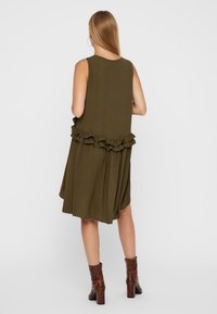 Mekko oliivinvihreä väri, jossa on liehuva muotoilu ja röyhelöhelma. Valmistettu kevyestä kankaasta, siinä on rento istuvuus ja olkaimeton tyyli.