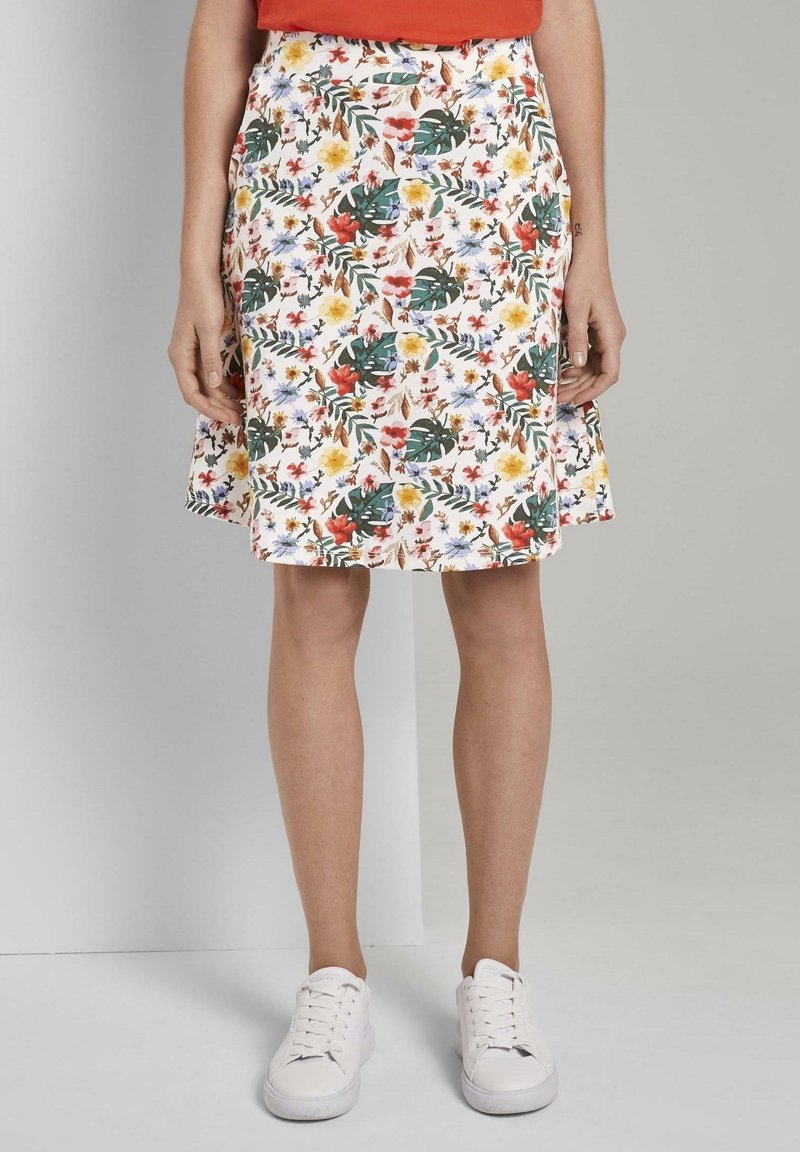 Jupe à motif floral mettant en avant des fleurs colorées et des feuilles vertes sur un fond blanc. Forme évasée, longueur au genou, avec un ourlet évasé.