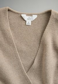 Maglione beige con scollo a V e trama a coste, etichetta con scritto "THE SET", taglia M, realizzato con tessuto morbido e lavorato a maglia, dal design semplice.