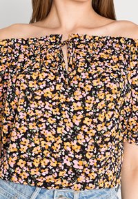 Haut noir à épaules dénudées avec des motifs floraux en rose, orange et vert. Présente un col froncé et des manches courtes bouffantes.