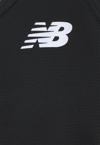 Svart atletisk tyg med en strukturerad yta och en framträdande vit New Balance-logotyp. Enkelt och strömlinjeformat design.