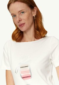 Biała koszulka z bawełny z drukowaną grafiką makaroników w pastelowych kolorach z napisem "Life is" powyżej, okrągłym dekoltem i krótkimi rękawami.