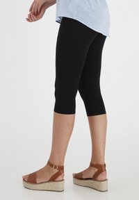 Czarne legginsy capri zestawione z brązowymi sandałami na koturnie z jutikową podeszwą. Stylizację dopełnia jasnoniebieska tunika.