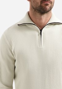 Geribbeld crèmekleurig pullover met een halve rits kraag. Heeft een tonale rits en een gestructureerde textuur, die een veelzijdig ontwerp benadrukt.