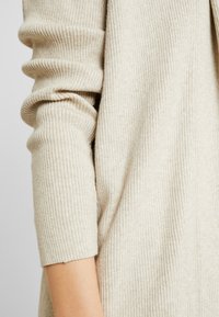 Beige ribbad tröja med långa, rynkade ärmar och mjuk textur, med en avslappnad passform och subtil färgvariation.