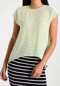 Ljusgrön chiffongblus med rundad halsringning och korta ärmar, med en längre bakfåll, i kombination med en svart och vit randig kjol.