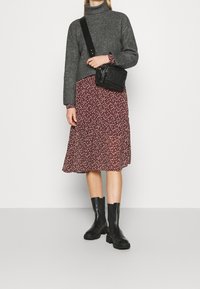 Suéter gris de cuello alto con canalé, vestido de flores en burdeos, bolso de bandolera negro y botines negros. Se aprecian materiales de mezclas texturizadas.