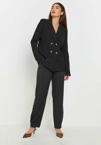 Zwarte dubbelzijdige colbert met gouden knopen, gecombineerd met bijpassende broeken. Compleet met puntige schoenen met luipaardprint.