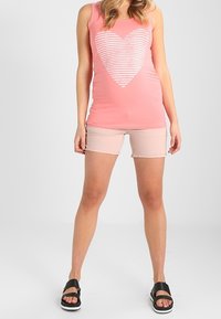 Pink tank top with white striped heart design, paired with light pink shorts and black slide sandals. Simple, casual outfit.