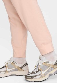 Sudadera de color rosa claro con puños de canalé, combinada con zapatillas deportivas blancas y plateadas que cuentan con paneles de malla y acentos dorados.