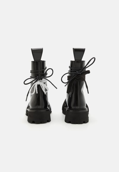 Botines negros de charol con suelas gruesas, que cuentan con cordones en blanco y negro contrastantes atados en la parte trasera y una pestaña rectangular para tirar.