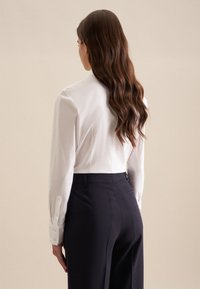 Biała koszula z długim rękawem i mankietami na guziki, zestawiona z ciemnymi, dopasowanymi spodniami. Koszula ma usztywnioną konstrukcję i gładką fakturę.