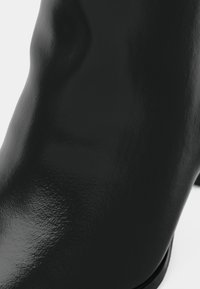 Μαύρο δερμάτινο μποτάκι αστραγάλου με γυαλιστερό φινίρισμα, με κομψό σχεδιασμό και καμπυλωτή σιλουέτα, που αναδεικνύει την απαλή υφή και τις καθαρές γραμμές.