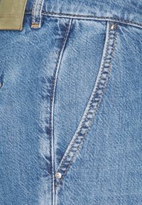 Siniset farkut, joissa on lähikuva vetoketjusta, näkyvistä saumoista, hopeanvärisestä napista ja teksturoidusta kangaskuvioinnista.