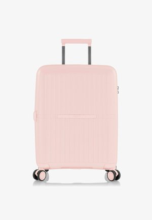 Valise rigide de couleur rose pastel, de forme rectangulaire, avec texture côtelée verticale, poignée rétractable et quatre roues pour la mobilité.
