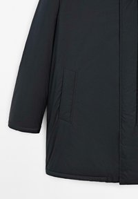 Schwarze Pufferjacke mit minimalistischem Design, langen Ärmeln, einem dezenten Glanz und zwei seitlichen Taschen mit gestickten Kanten.