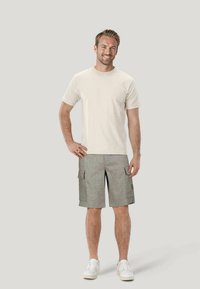 Maglietta beige e pantaloncini cargo grigio chiaro con tasche laterali, realizzati in tessuto morbido; modello con indosso sneakers bianche, in piedi su uno sfondo neutro.