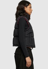 Sort puffer vest med høy krage, sidelommer og kontrastfarget rosa søm. Designet er cropped med en boksformet silhuett.