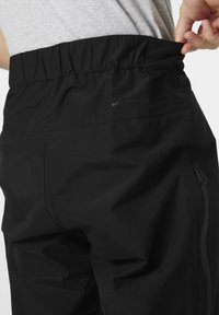 Zwarte waterdichte broek met een elastische tailleband, zijzakken met rits en subtiele branding. Soepele textuur met een matte afwerking.