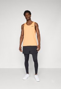 Orange ærmeløs tanktop med "BORG" logo, parret med sorte shorts og leggings. Hvide sportsko fuldender det sporty outfit.