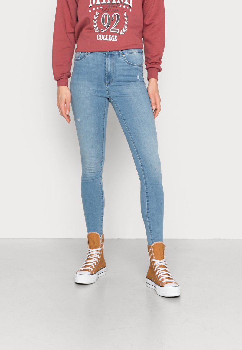Jeans ajustados de denim azul claro con ligero desgaste. Combinados con zapatillas altas en color beige con suelas y cordones blancos.