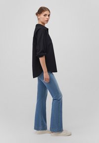 Black oversized shirt with rolled sleeves; paired with flared light blue jeans and white sneakers. Simple design, cotton material.