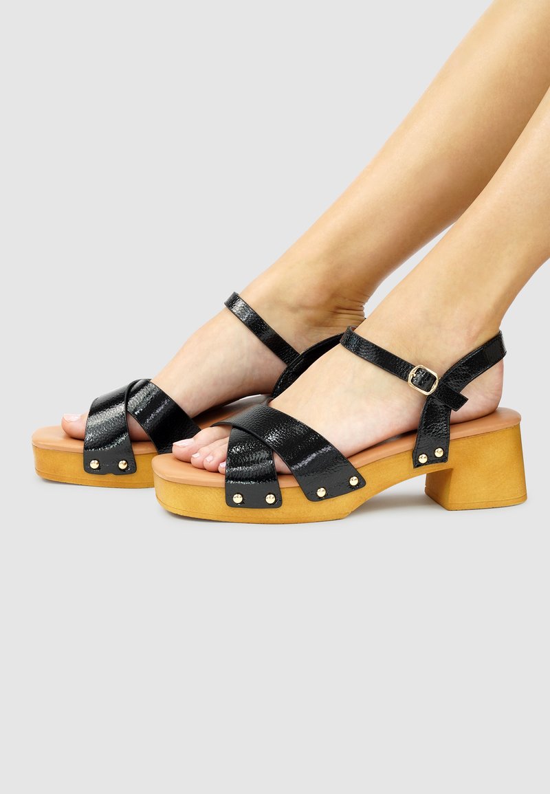 Zwarte sandalen met bandjes en een gestructureerde afwerking, voorzien van een stevige beige blokhak, een verstelbare enkelriem en accenten in gouden tint.