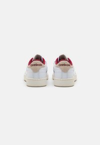 Weiße Ledersneaker mit bordeauxroten Akzenten, beigen Gummisohlen und sichtbarem Reebok-Branding an der Ferse und am Rückenteil.