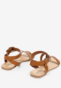 Sandalias de piel sintética marrón con un diseño de punta abierta, que presentan cintas cruzadas y un cinturón en el tobillo. Plantilla texturizada y suela plana.