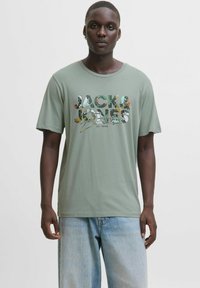 Gaiši zaļš kokvilnas T-krekls ar "JACK & JONES" grafiku daudzkrāsainā drukā. Īsas piedurknes un apaļš kakls, saskaņots ar brīvām džinsām.