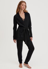 Zwart gebreid loungewear set met een wikkelcardigan met een strikceintuur, patchzakken en bijpassende slim-fit broek met omgeslagen enkels.