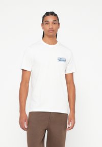 Biała bawełniana koszulka z niebieskim logo "Rip Curl" na lewej piersi, okrągłym dekoltem i krótkimi rękawami. Gładka struktura.