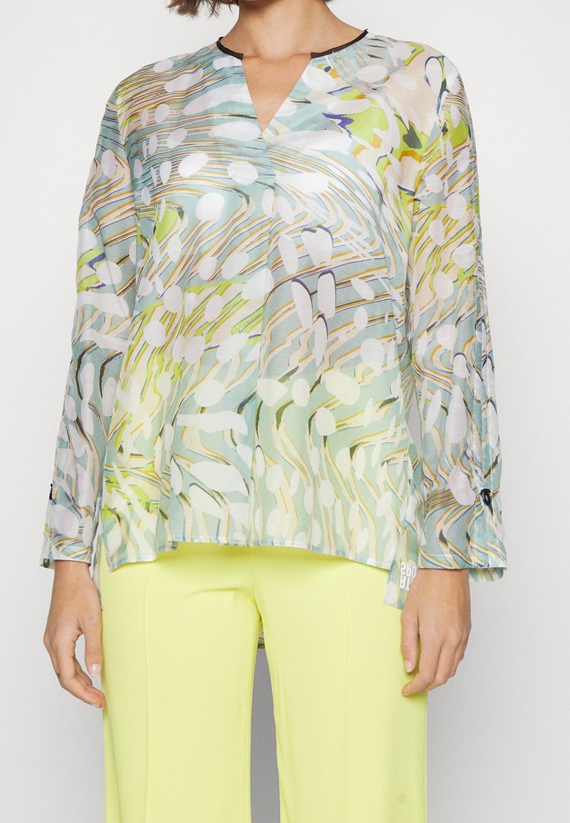 Florale, leichte Bluse mit V-Ausschnitt, langen Ärmeln und gemischten Farben in Grün, Gelb und Weiß mit abstrakten Mustern.