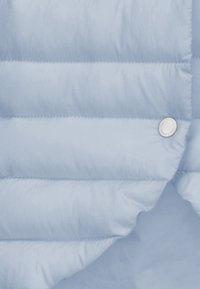 Hellblaue Steppjacke aus einem Stoff mit horizontalen Steppnähten, glatter Textur und einem silbernen Druckknopfdetail an der Vorderseite.