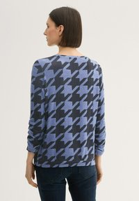Langärmliges Oberteil mit blauem und schwarzem Hahnentrittmuster, Rundhalsausschnitt und hochgekrempelten Ärmeln, aus einem weichen Material gefertigt.