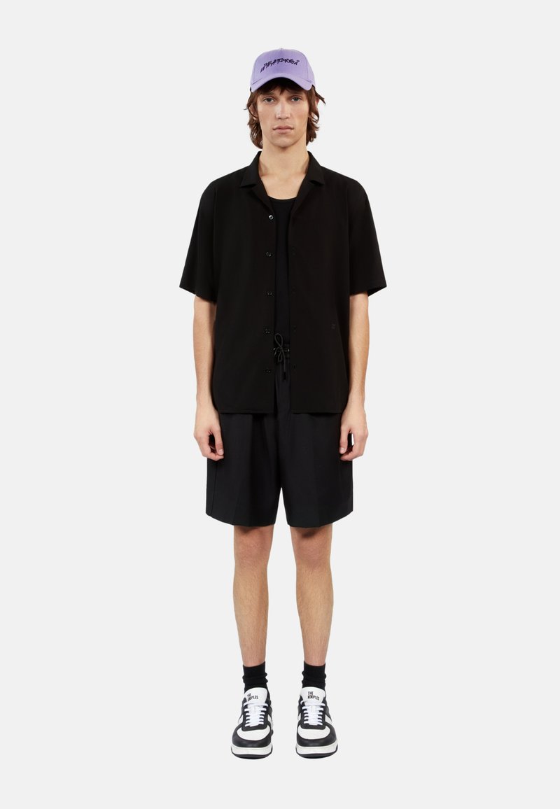 Zwarte korte mouwen overhemd over een zwart tanktop, gecombineerd met zwarte shorts. Lichtpaarse pet en zwart-witte sneakers.
