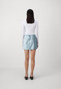 Ljusblå denim mini kjol med hög midja, rak skärning och fransad nederkant. Tillsammans med en långärmad vit topp och svarta skor med blockklack.