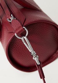 Round burgundy leather bag with textured finish, silver hardware, and a zipper closure. Features a detachable clip and leather strap.