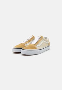 Zapatillas de gamuza marrón y tela crema con cordones blancos, ribete negro y suela de goma. Silueta clásica de corte bajo con diseño de franjas laterales.