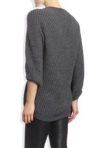 Personne portant un pull en grosse maille gris foncé avec de larges manches trois-quarts et un pantalon en cuir noir, vue de dos.