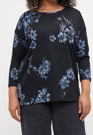 Zwart langemouwen top met blauw en witte bloemenprints, gedragen met donkergrijze broeken, model getoond van schouders tot heupen.