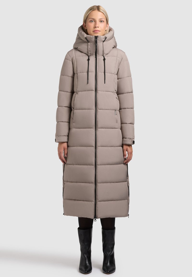 Cappotto lungo imbottito color beige chiaro con cappuccio, caratterizzato da pannelli imbottiti verticali, cerniere frontali e coulisse regolabili.