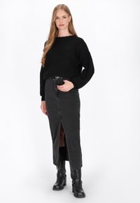 Pulover tricotat negru, cu o croială largă, asortat cu o fustă din denim neagră, cu talie înaltă, care are o despicătură frontală, și cizme negre cu cataramă până la gleznă.